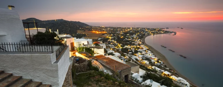 Dusk view of a coastal village on Euboea Island, Greece, with illuminated hillside houses and a bay